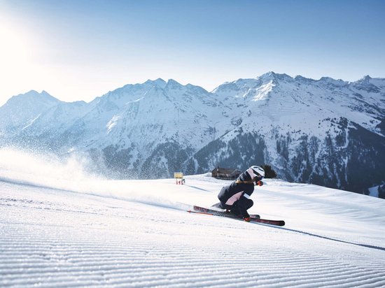St. Anton: Sommerurlaub, Winterspaß Skifahrer auf präparierter Piste mit verschneiten Bergen im Hintergrund