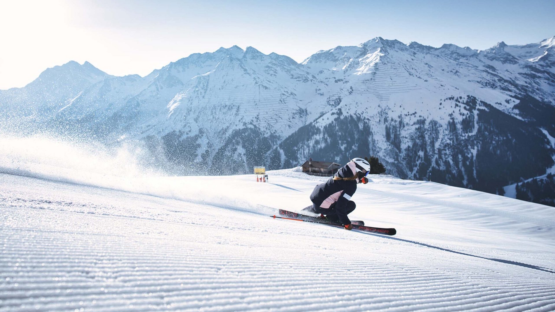 Skifahrer auf präparierter Piste mit verschneiten Bergen im Hintergrund