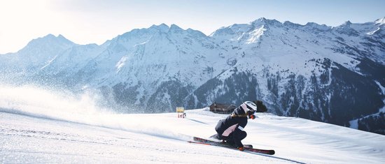 Skifahrer auf präparierter Piste mit verschneiten Bergen im Hintergrund