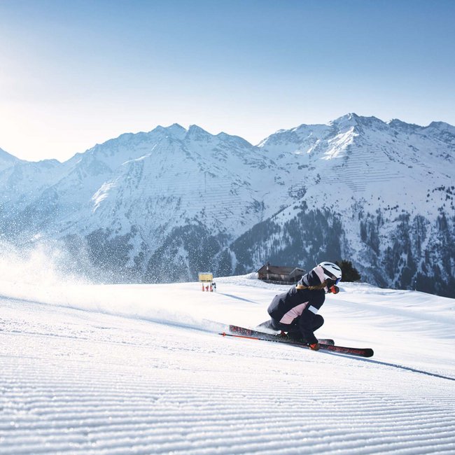 Skier on groomed slope with snowy mountains in the background