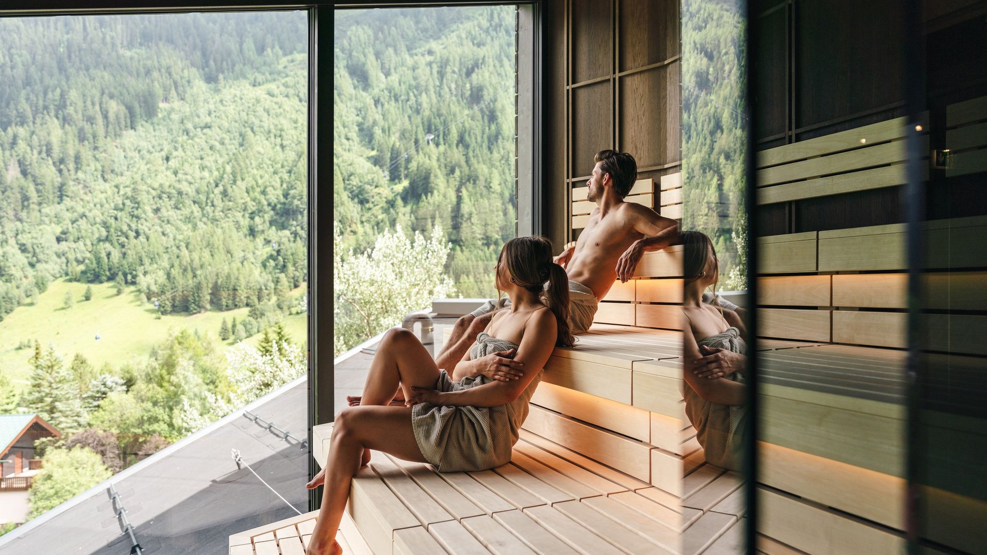 Couple relaxing in sauna with view of forested mountains