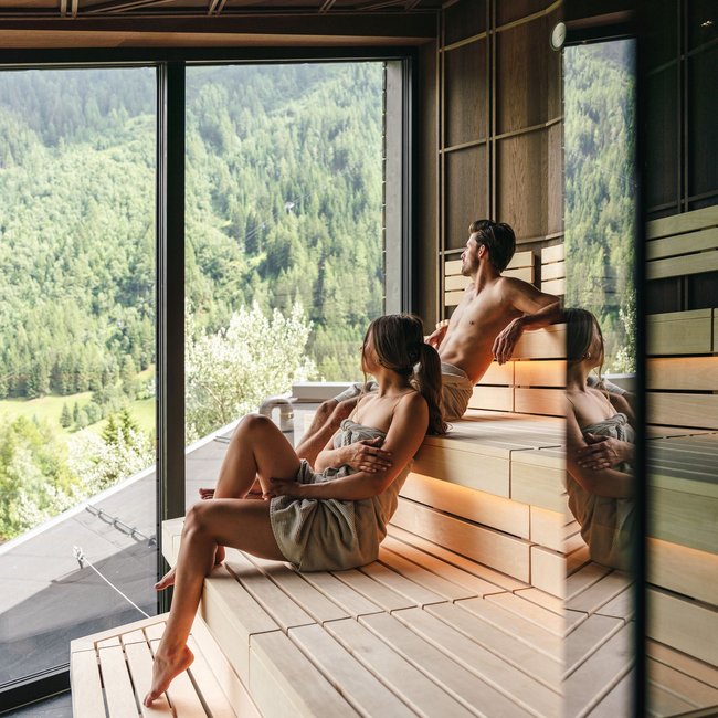 Paar entspannt in Sauna mit Blick auf bewaldete Berge