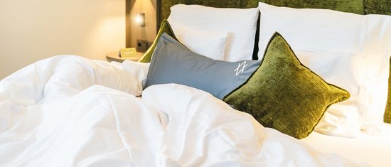 Gemachtes Bett mit weißen Laken und grünen Kissen vor grünem Polsterkopfteil