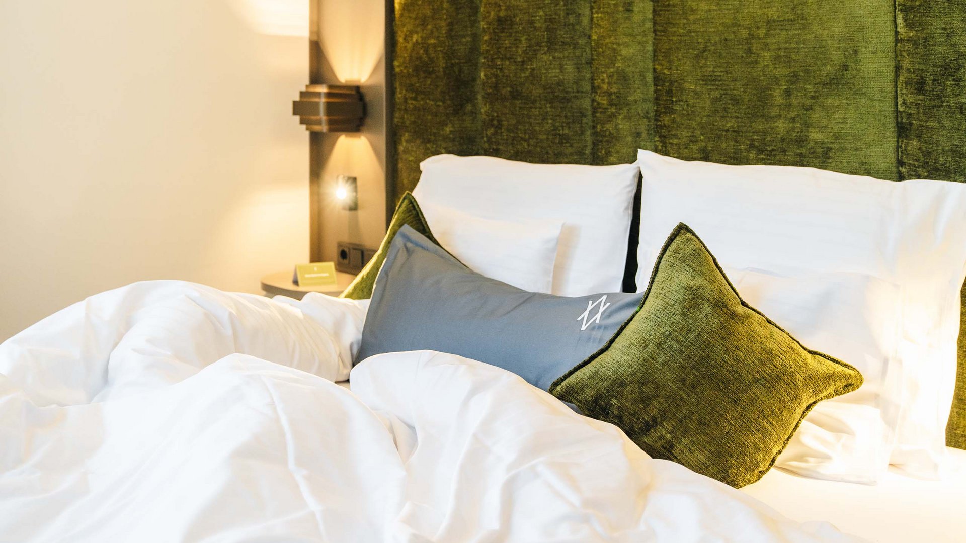 Made bed with white sheets and green pillows against a green upholstered headboard