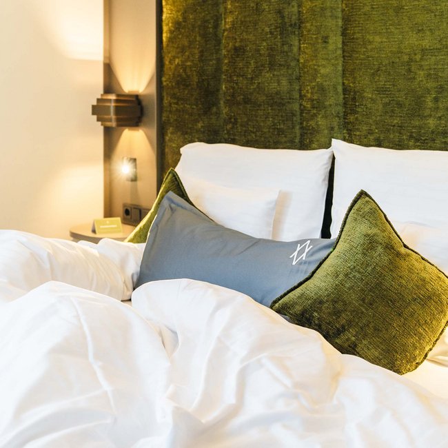 Gemachtes Bett mit weißen Laken und grünen Kissen vor grünem Polsterkopfteil