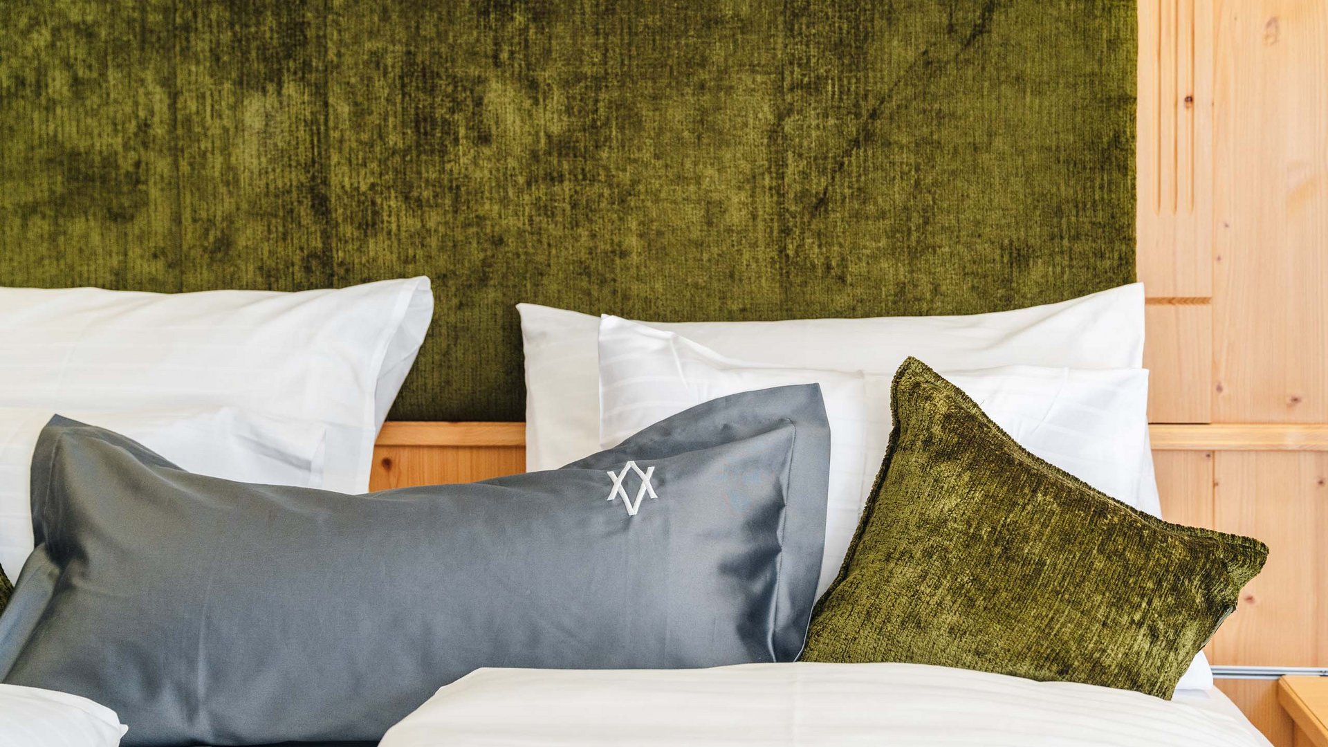 White bed with green and gray pillows against green upholstered headboard