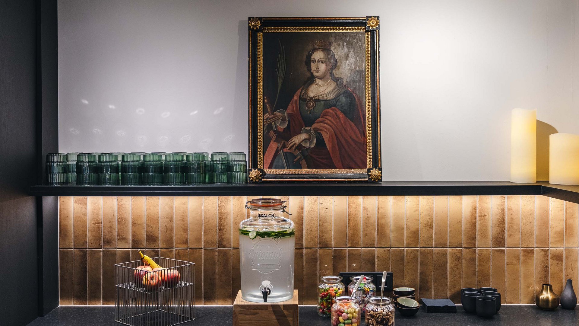 Counter with water dispenser, glass jars, fruit basket, and historic painting on wall