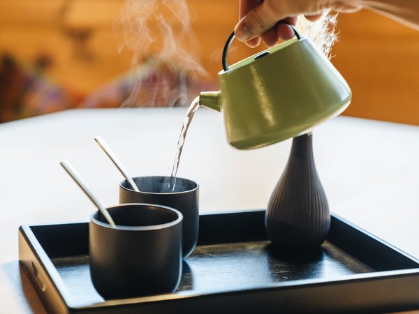 Hot water pouring from teapot into two black cups on tray