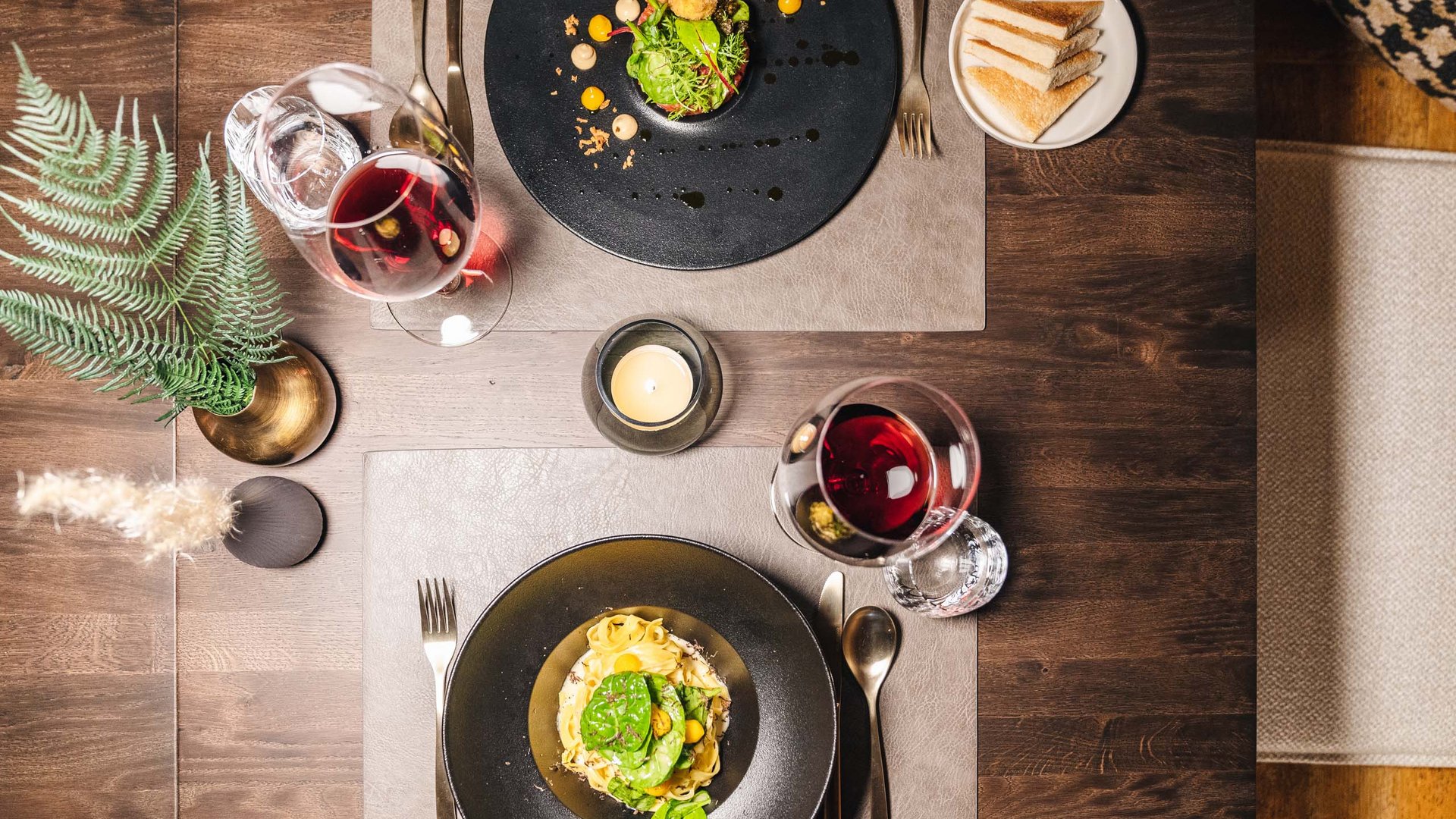 two plates with fine food, wine glasses, and bread slices on wooden table