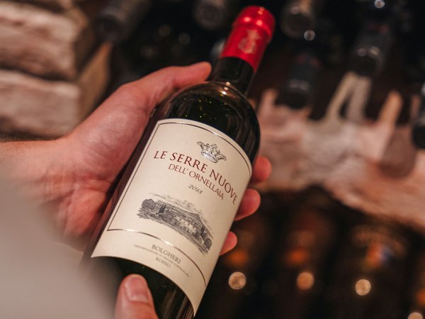 Hand hält eine Flasche Le Serre Nuove Rotwein aus einem Weinkeller