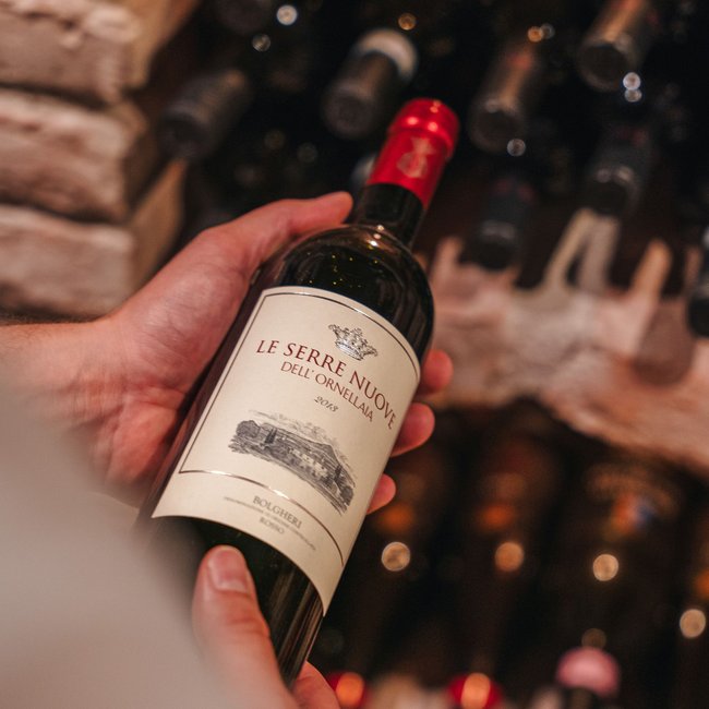 Hand hält eine Flasche Le Serre Nuove Rotwein aus einem Weinkeller