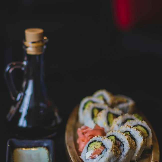 Sushi-Rollen mit Avocado und Lachs auf Holzbrett mit Sojasauce und Ingwer