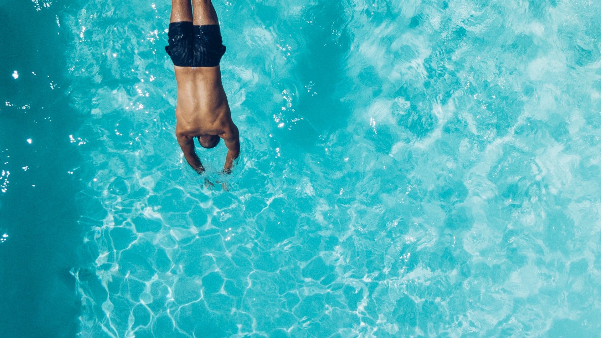 Man diving headfirst into clear blue water of a swimming pool
