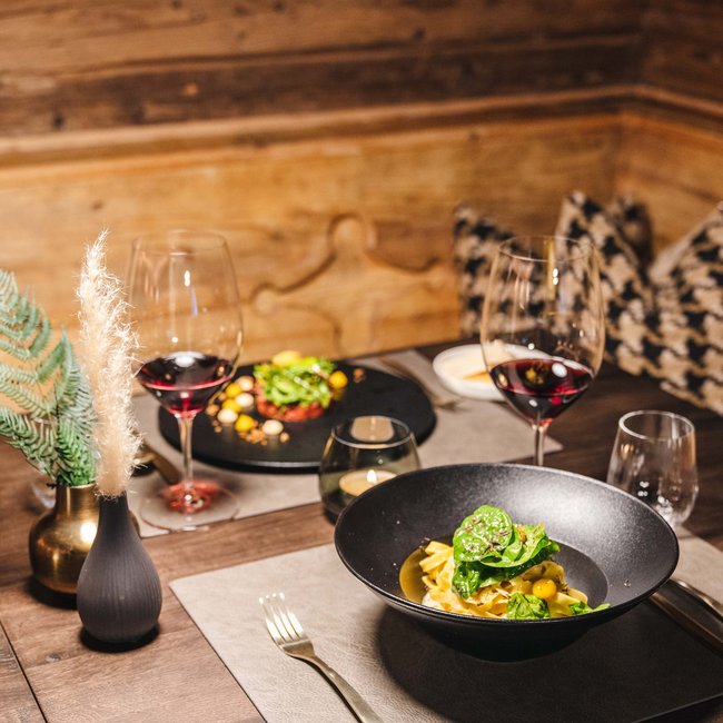 Bezauberndes Wellnesshotel in St. Anton/Tirol Gemütlicher Esstisch mit Pasta, Salat und Rotwein in einer Holzeinrichtung