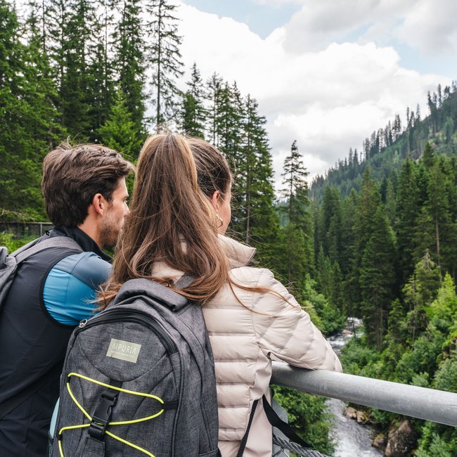 Arpuria is your bike hotel in Tyrol Couple with backpacks overlooking river and forest in the mountains