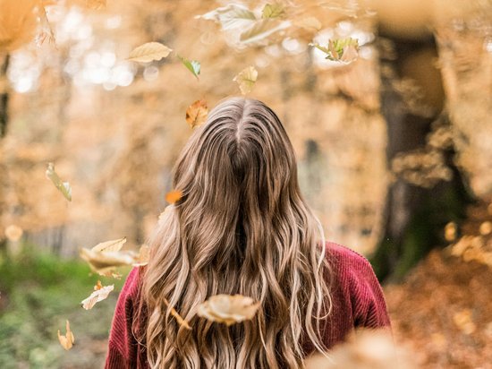 Ein echter Kick und jede Menge Spaß Frau mit langen blonden Haaren in rotem Pullover im Herbstwald mit fallenden Blättern