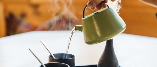 Heißes Wasser wird aus einer grünen Teekanne in schwarze Tassen gegossen