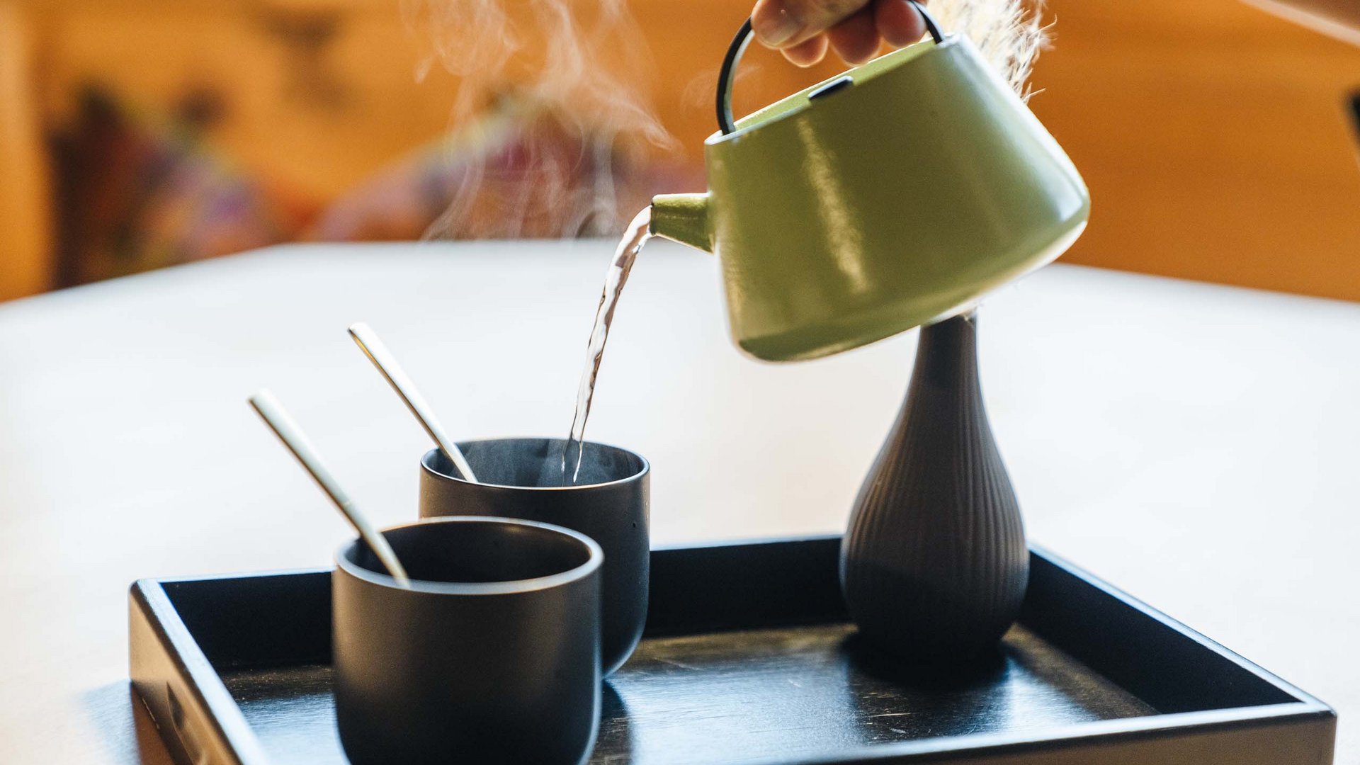 Hot water poured from a green teapot into black cups