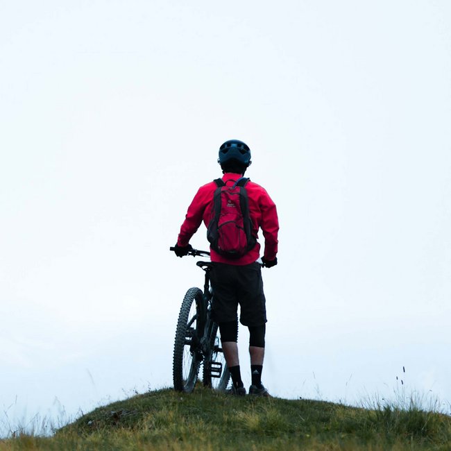 Ihr Bikeurlaub in Tirol Mountainbiker steht mit Fahrrad auf grasigem Hügel vor hellem Himmel