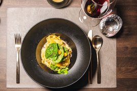 Pasta with spinach leaves and yellow tomatoes in black bowl with red wine