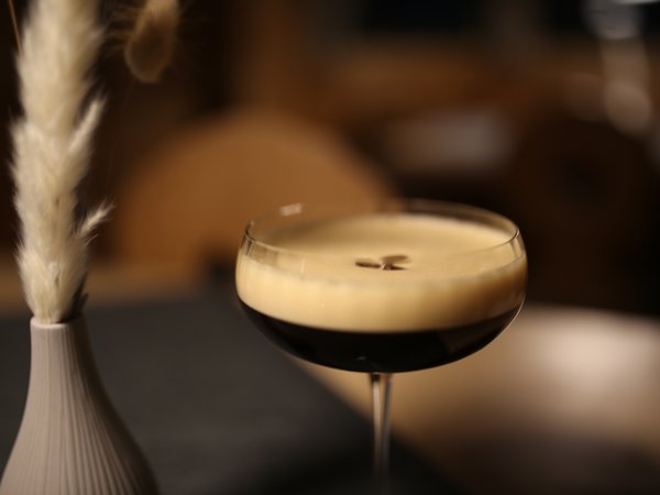 Espresso Martini in glass with foam and coffee beans on dark brown background