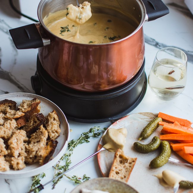 Cheese fondue with bread, pickles, carrots, and garlic on marble table