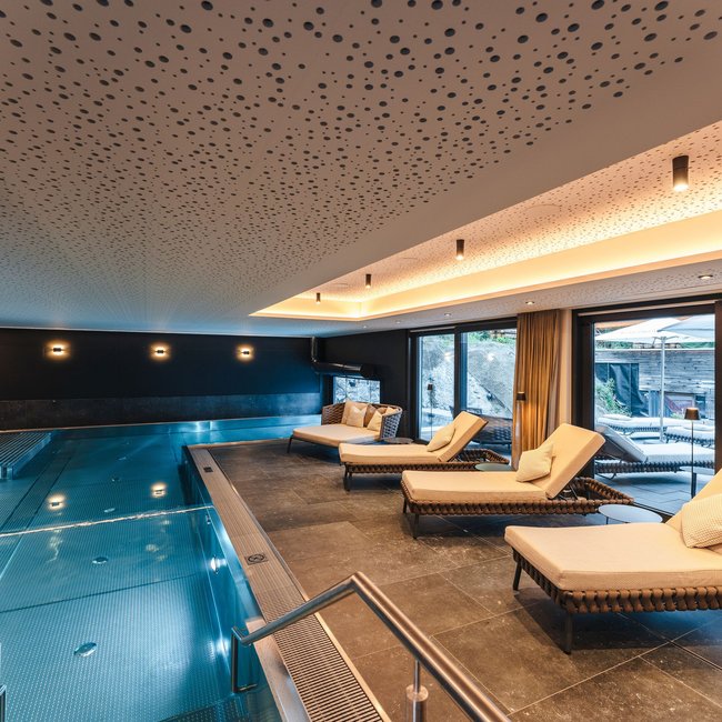 Welcome to your holiday on Arlberg – in summer and winter Modern indoor pool with lounge chairs and large windows opening to a terrace