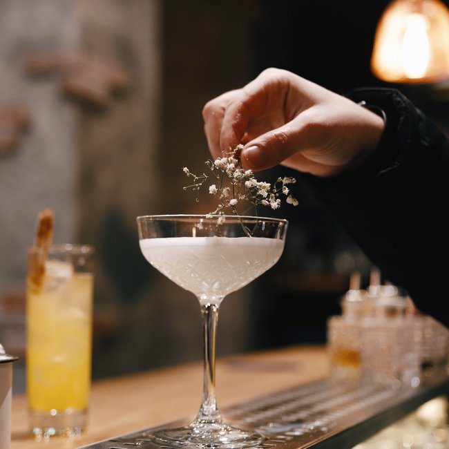 Hand decorating white cocktail with small flowers in bar