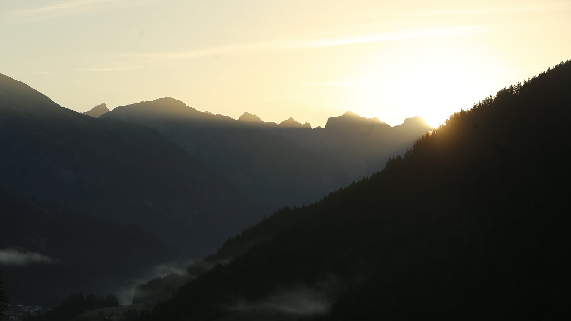 Sonnenaufgang hinter bewaldeten Bergen mit Nebel im Tal