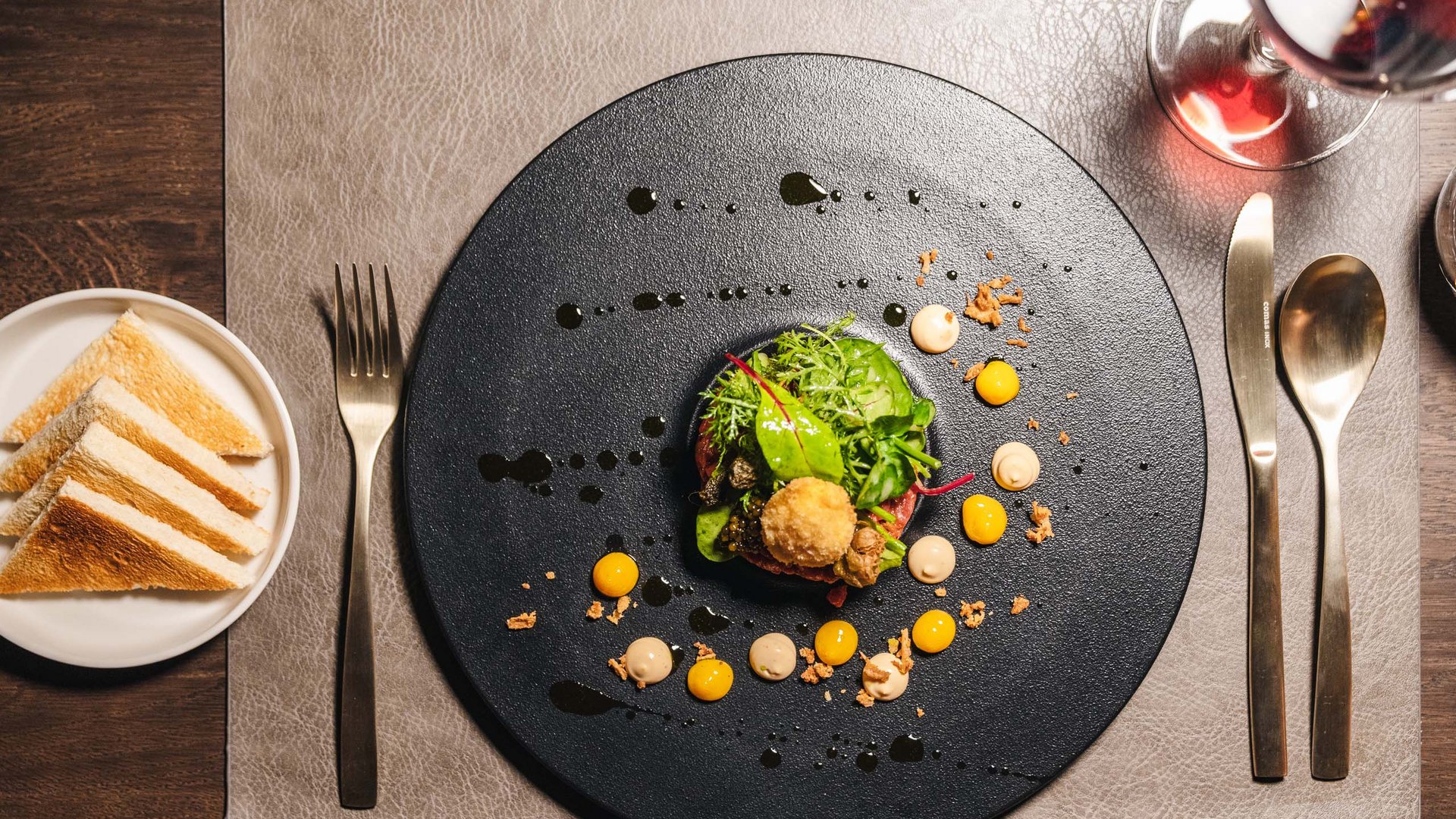 Gourmet appetizer with salad and sauce dots on a black plate