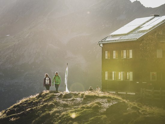 Hikers near a mountain hut with sunlight and mountains in the background