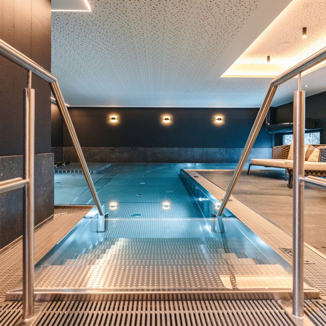 Innenaufnahme eines modernen Schwimmbads mit beleuchteten Stufen und Lounge-Bereich