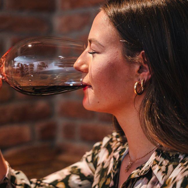 Frau trinkt Rotwein in einem Glas vor einer Ziegelsteinwand