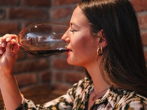 Frau trinkt Rotwein in einem Glas vor einer Ziegelsteinwand