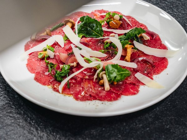 3 restaurants under one roof Carpaccio with mushrooms, arugula, and parmesan shavings on white plate