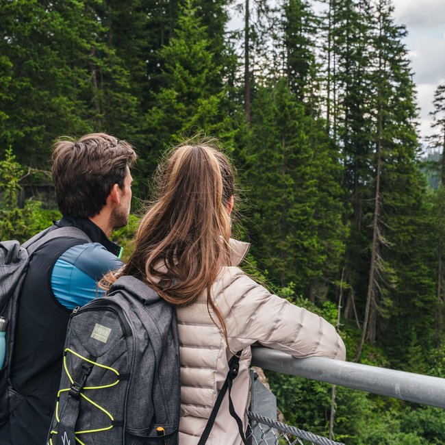 Paar betrachtet Fluss und Wald auf einer Brücke im Gebirge