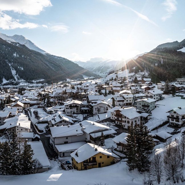 Sonnenaufgang über verschneitem Bergdorf im Tal zwischen Bergen