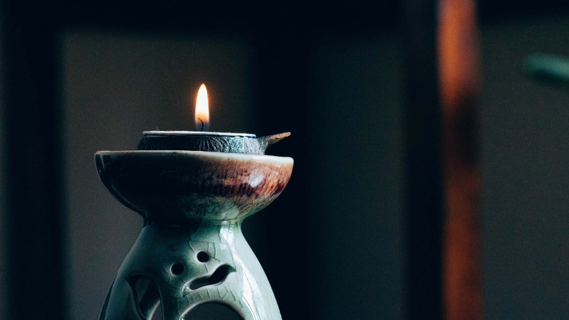 Lit candle on a decorative green ceramic lamp in a dark room