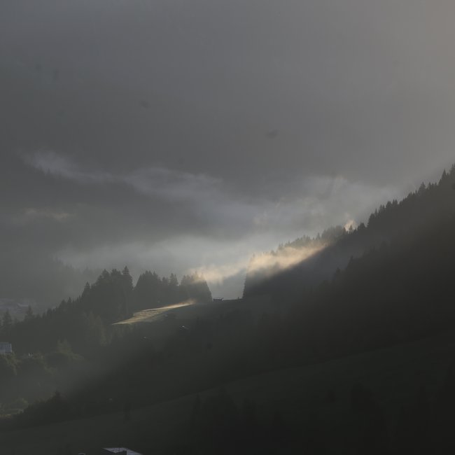Sonnenlicht durch brüchige Wolken über bewaldeten Hügeln