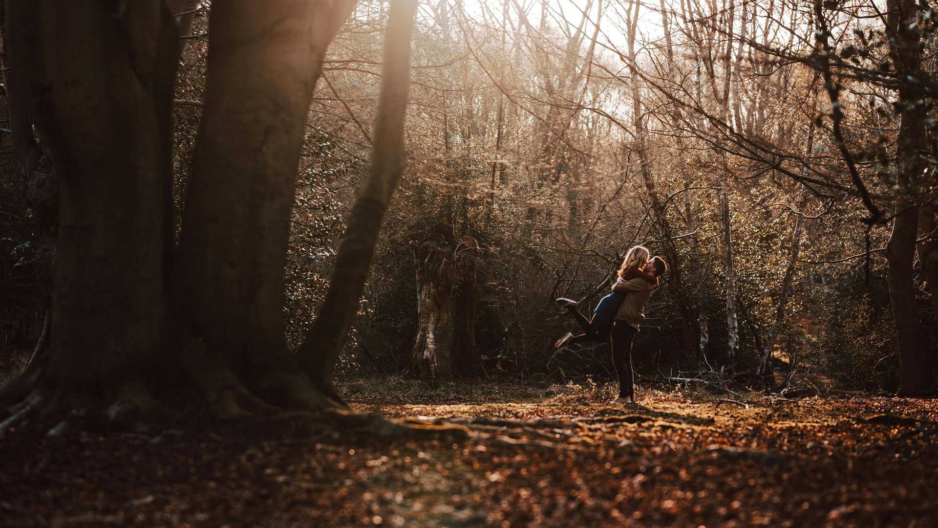 Couple embracing happily in autumn forest with sunlight filtering through trees