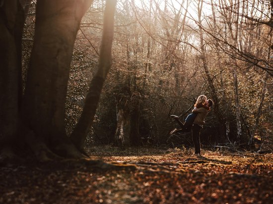 Couple embracing happily in autumn forest with sunlight filtering through trees