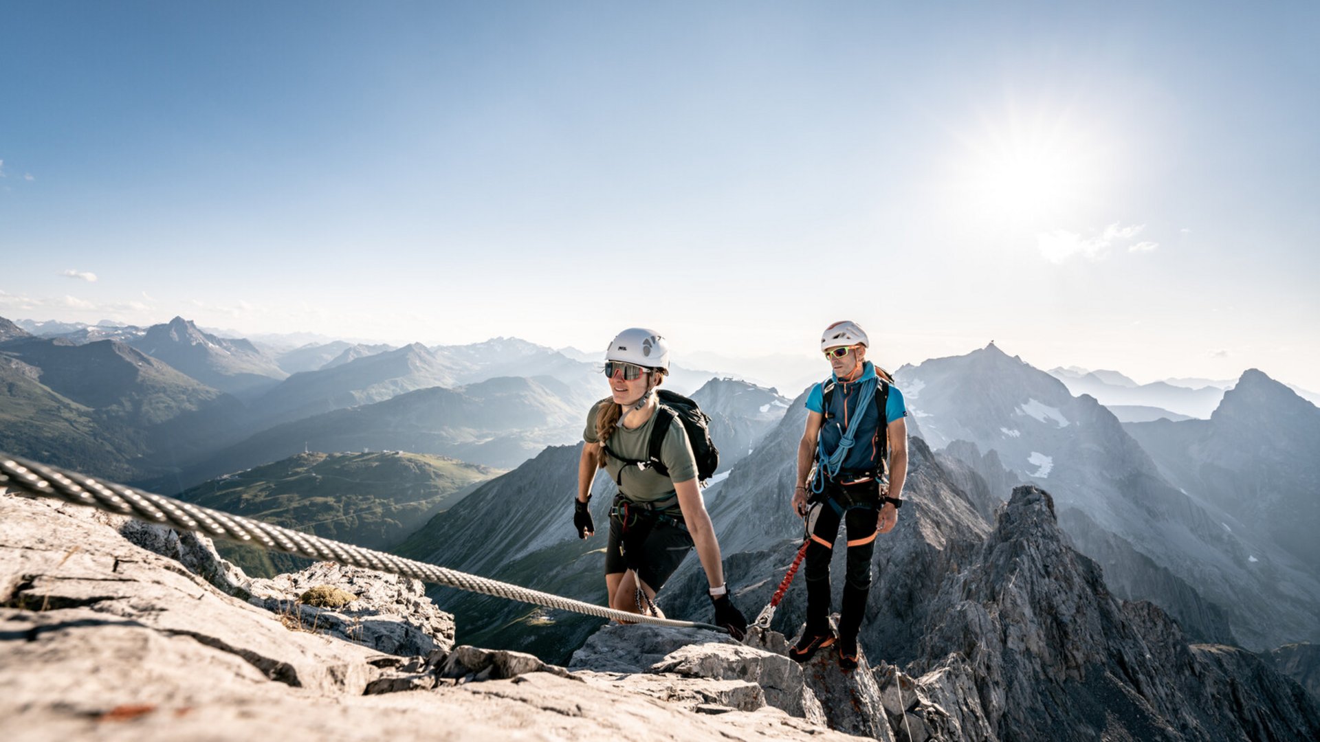 Two climbers ascending with safety gear in a sunny mountain landscape