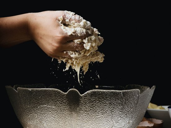 St. Anton: Sommerurlaub, Winterspaß Hand knetet Teig über einer Glasrührschüssel auf Holztisch