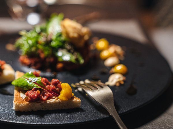 3 restaurants under one roof Gourmet dish with toast, raw meat, green leaves, and sauces on a black plate