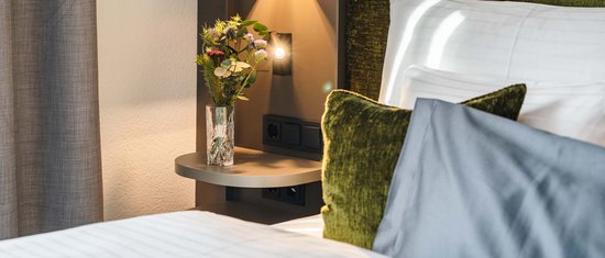 Schlafzimmer mit grünem Kopfteil, Kissen und Nachttisch mit Vase und Blumen