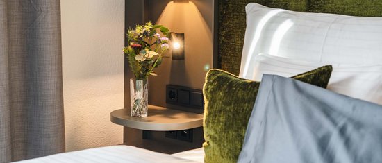 Bedroom with green headboard, pillows, and bedside table with vase and flowers