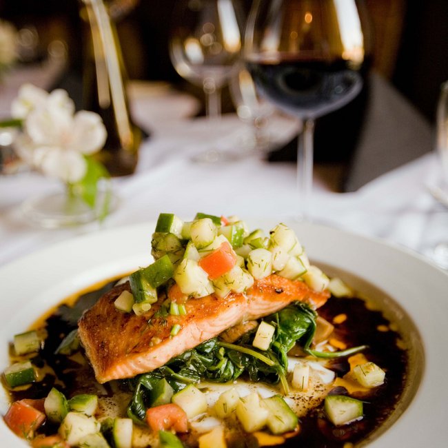 Grilled salmon fillet with vegetables on plate, glass of red wine in background